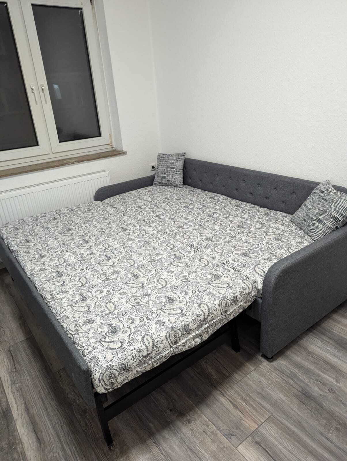 Un lit avec une couvre-lit à motifs, une tête de lit rembourrée de couleur grise et deux oreillers.