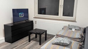 Un soggiorno moderno con una TV nera su un mobile, un divano grigio con cuscini a righe, un tavolino nero e una finestra con vista.