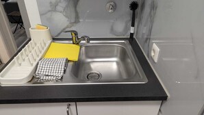 Una cucina con un lavello in acciaio inox, una spugna gialla, un espositore per piatti bianco e uno strofinaccio a quadretti.