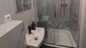 Un bagno moderno con doccia vetro, lavabo bianco e specchio soprastante.