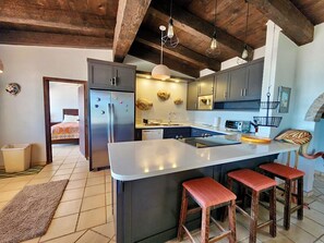 Kitchen features a central island with sink and bar stools, stainless steel appliances, and a large window.