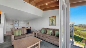 A modern living room with a sofa, coffee table, and a kitchen in the background. - White Crystal 209- ski-in ski-out (Mount Hotham)