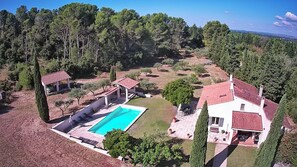 A large house with a swimming pool, surrounded by trees and a hilly landscape.