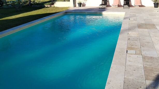 Una piscina rettangolare con acqua cristallina, circondata da un solarium piastrellato.