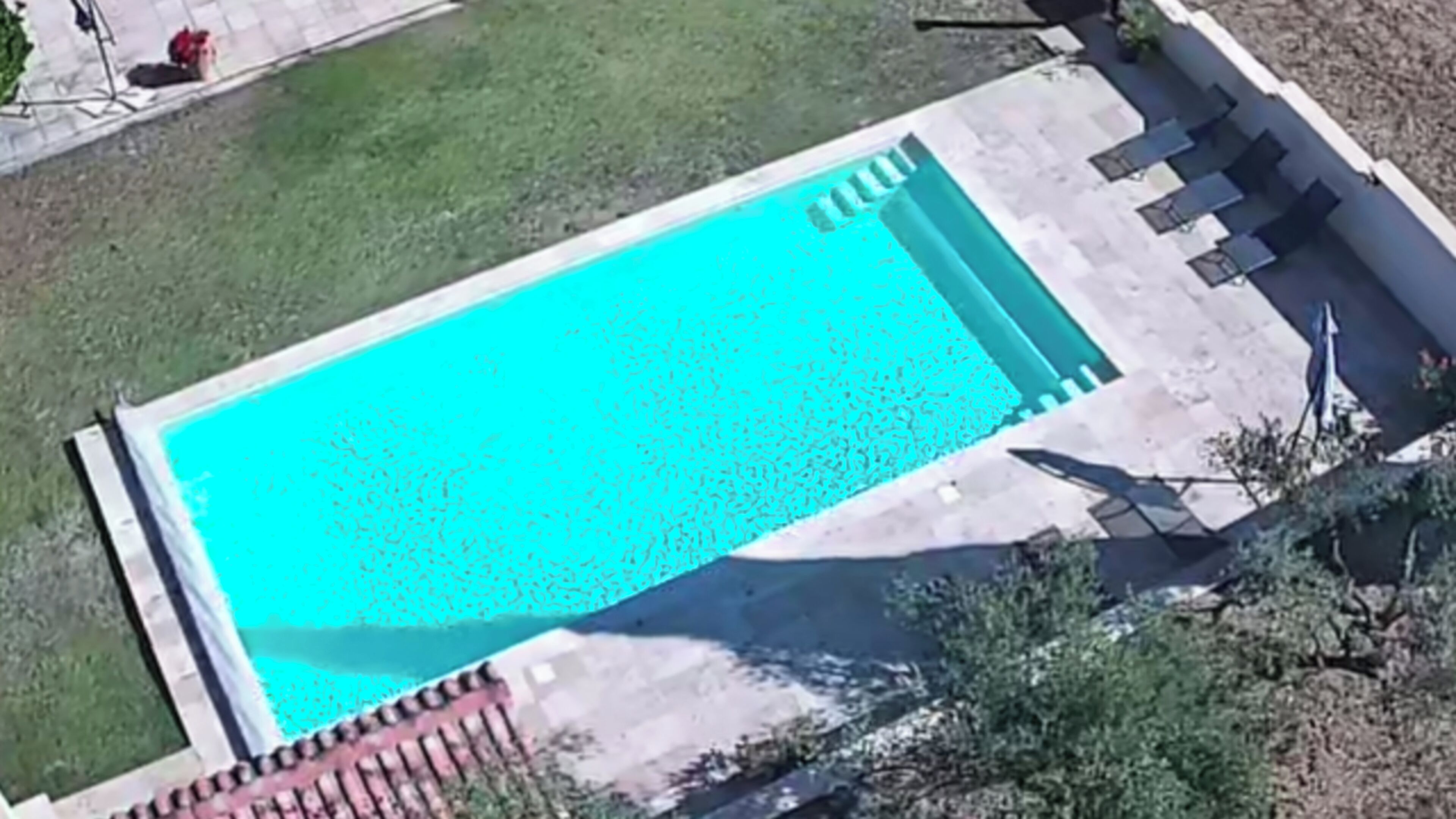 Et rektangulært pool med fliseterrasse og en lille græsplæne omkring.
