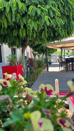 Un espacio al aire libre cubierto con mesas y sillas, rodeado de follaje y una jardinera roja.