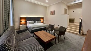 Une chambre d’hôtel avec un lit, un canapé, une table basse et un bureau. Un escalier mène à un étage supérieur.