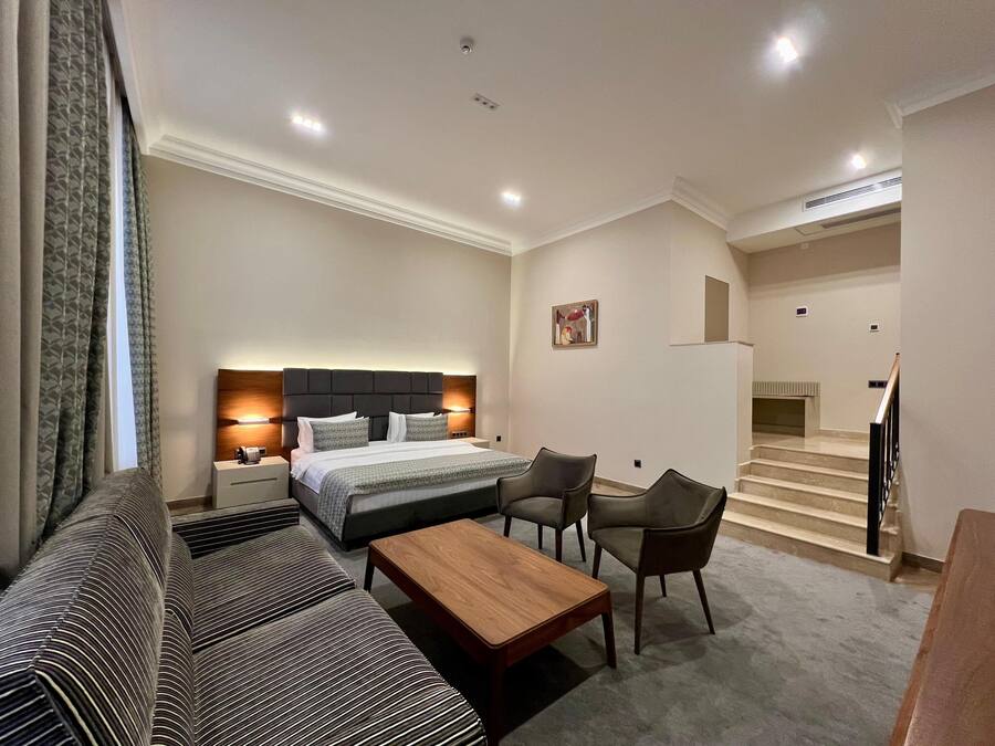 Ein Hotelzimmer mit einem Bett, einer Couch, einem Couchtisch und einem Schreibtisch. Eine Treppe führt zu einer oberen Ebene.