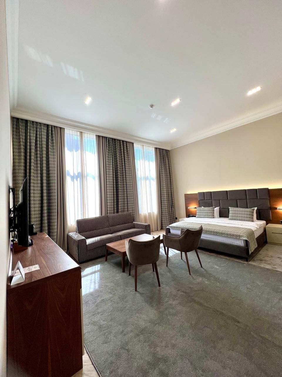 A modern hotel room with a large bed, a sofa, a desk, and a small table.