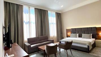 A modern hotel room with a large bed, a sofa, a desk, and a small table.