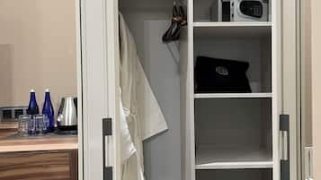Ein begehbarer Kleiderschrank mit Regalen, einem aufgehängten Bademantel und einer Mikrowelle auf der obersten Ablagefläche.