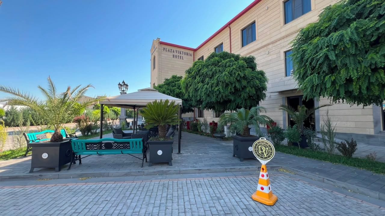 Un patio de hotel con mesas al aire libre, un mirador y un árbol grande.