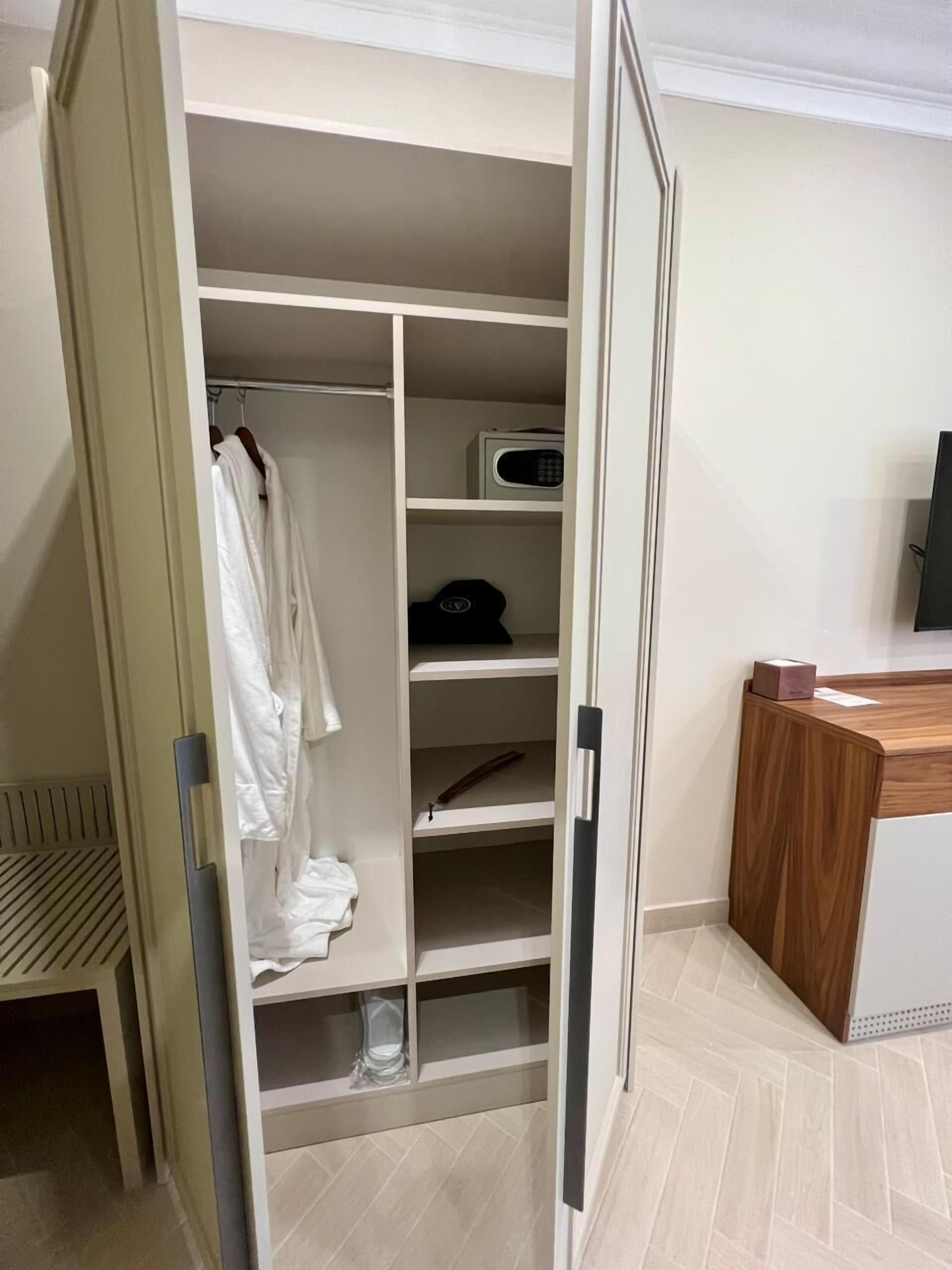 A walk-in closet with multiple shelves, a hanging rod, and a microwave.
