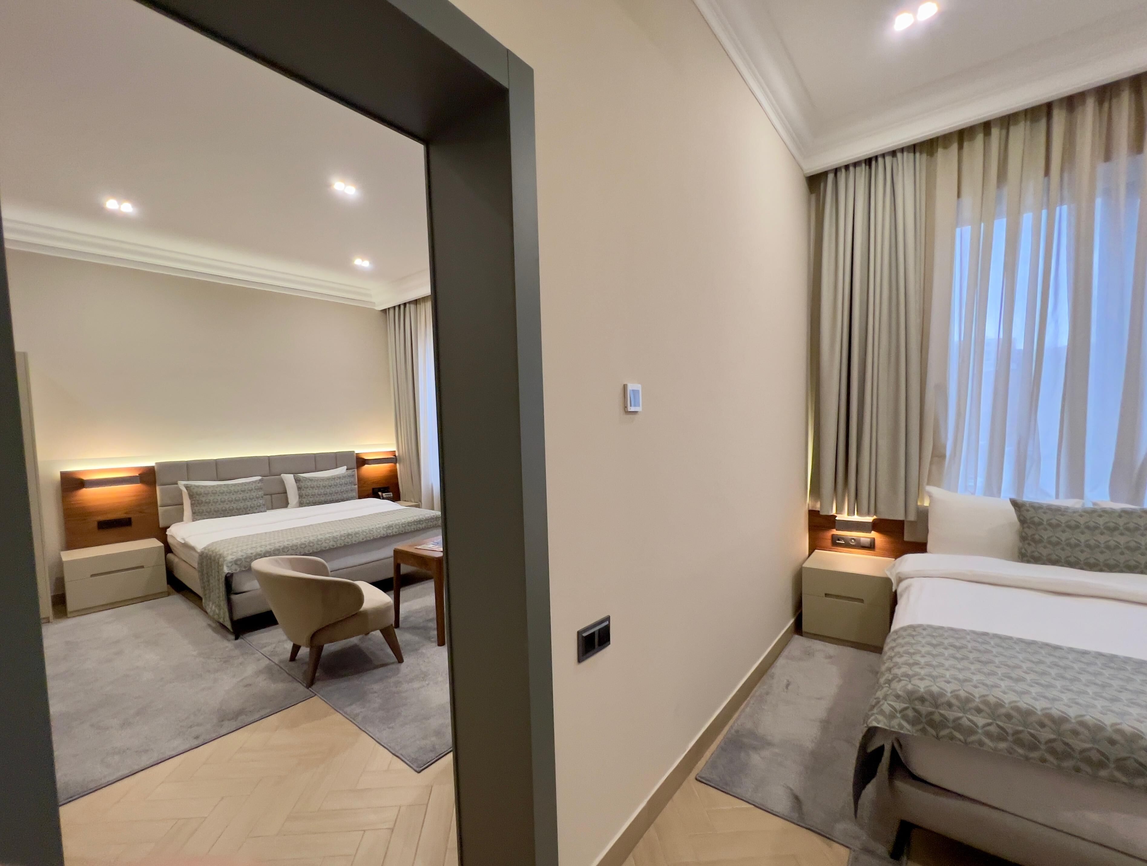 A hotel room with two beds, a desk, a chair, and a window with curtains.