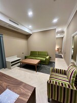 Een gezellig, ruimtelijk interieur met een groene bank, een gestreepte fauteuil, een houten salontafel en een witte bankje.