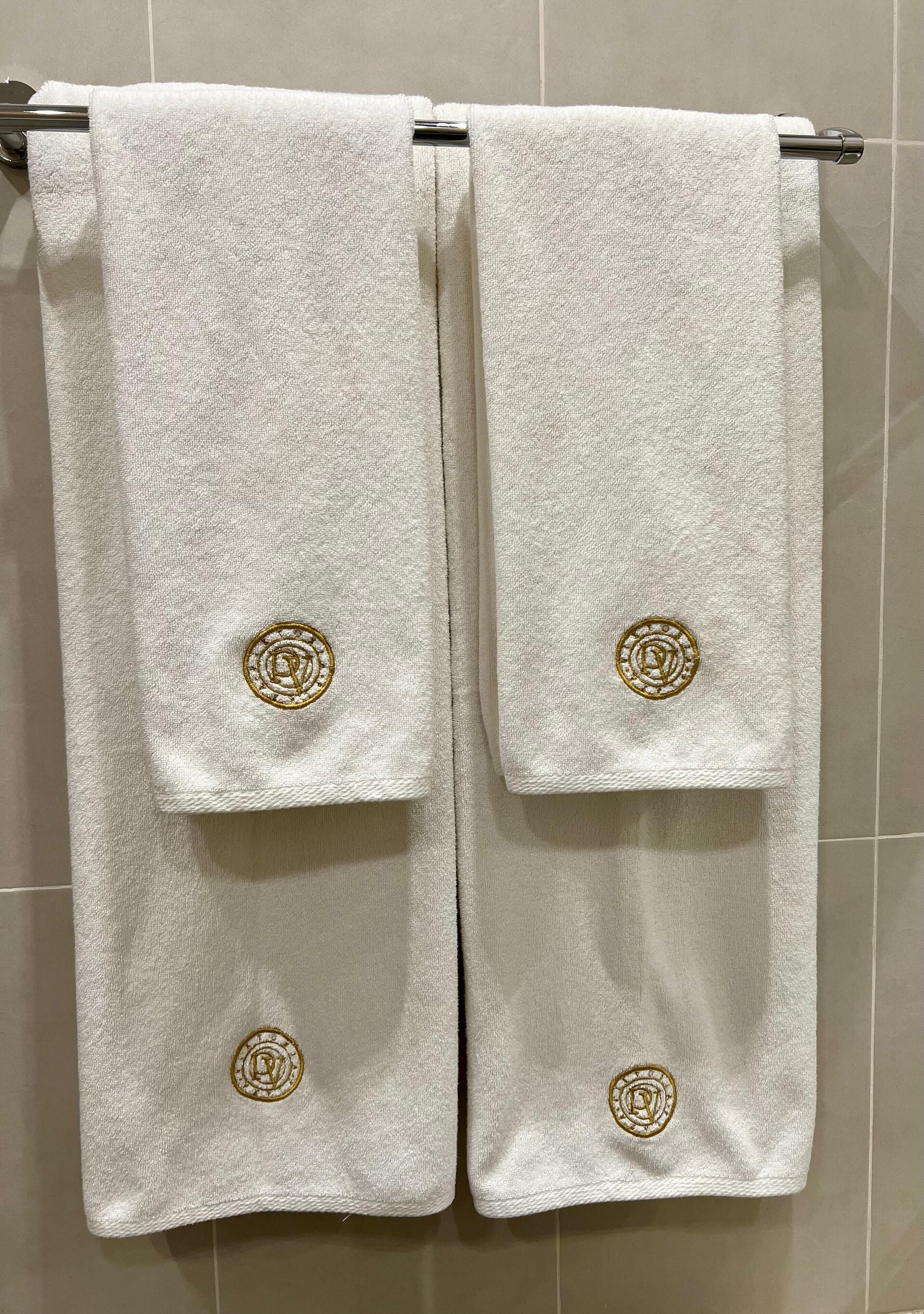 Two white towels with gold embroidery hanging on a metal towel rack.