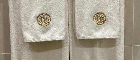 Two white towels with gold embroidery hanging on a metal towel rack.