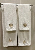 Twee witte handdoeken met gouden borduursel hangend aan een metalen handdoekhouder.
