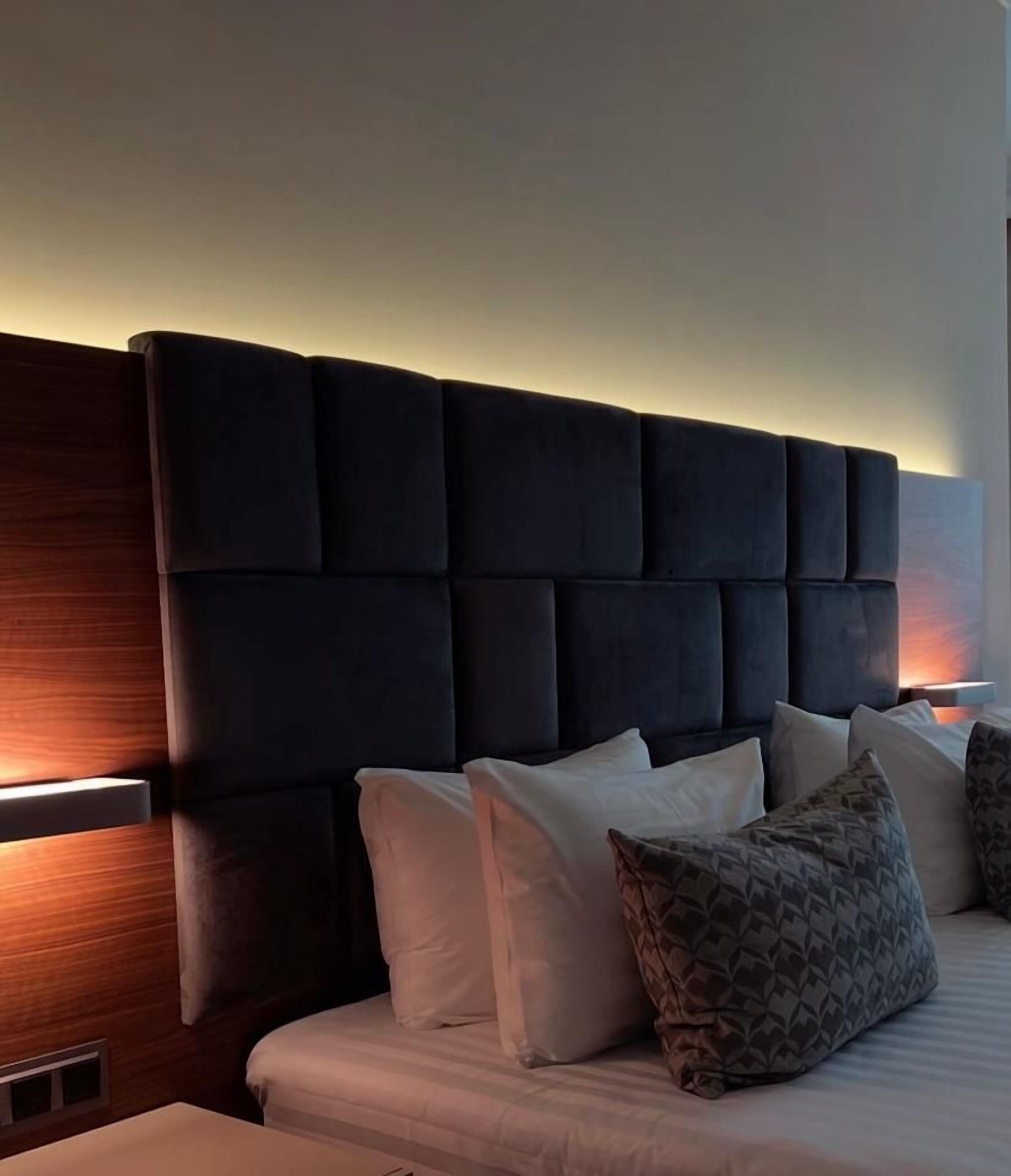 Une chambre à coucher moderne avec une tête de lit capitonnée, une table de chevet et un lit agrémenté de plusieurs coussins.