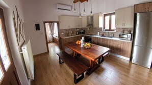 A modern kitchen with wooden cabinets, a stainless steel refrigerator, a wooden dining table with benches, and hanging pendant lights. - Anasa Residence (Chania)