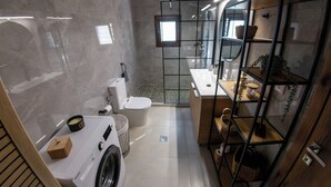 A compact bathroom with a washing machine, toilet, and glass-enclosed shower. - Anasa Residence (Chania)