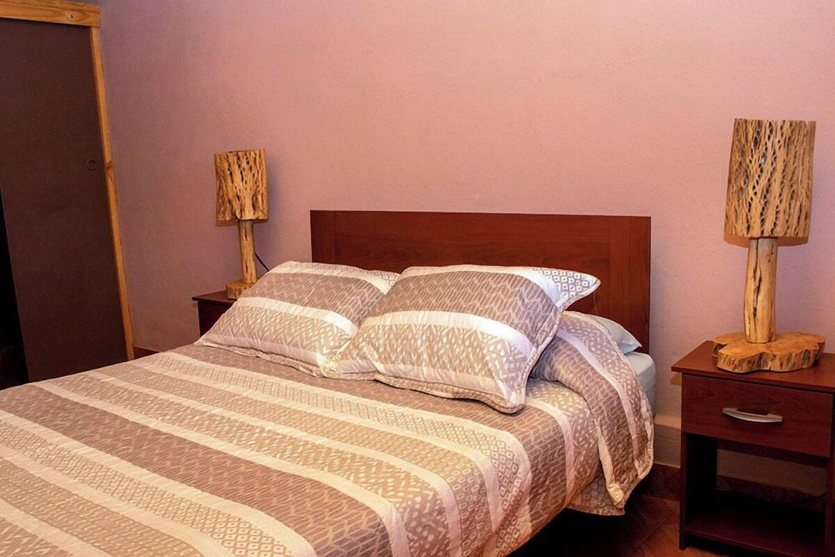 A neatly made bed with patterned bedding, two bedside tables with lamps, and a wooden headboard.