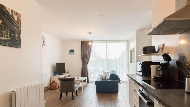 A modern kitchen with a stove, microwave, and utensils. There is a dining area with a table and chairs, and a living room with a sofa. - Le Gîte Saint-Jean - Caignac (Caignac)