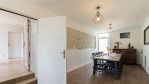 A dining area with a wooden table and chairs, a stone wall, and pendant lighting. - Le Gîte Saint-Jean - Caignac (Caignac)