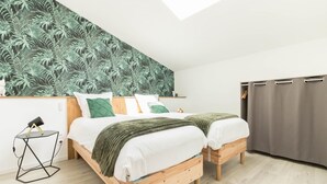 A bedroom with two beds, a skylight, a small table with a lamp, and a grey curtain. - Le Gîte Saint-Jean - Caignac (Caignac)