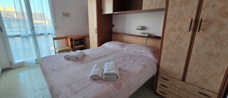 A hotel room with a bed, a wardrobe, a desk, and a chair.