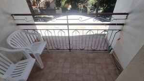 Un balcone con pavimento piastrellato, un cancello in metallo e due sedie in plastica bianca.
