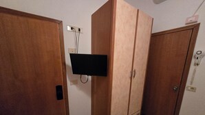 Una stanza con un armadio in legno, una TV a schermo piatto fissata al muro e un telefono.