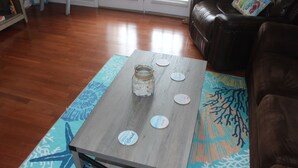 Une table basse en bois, sur laquelle reposent un bocal en verre et des sous-verres, le tout posé sur un tapis à motifs.