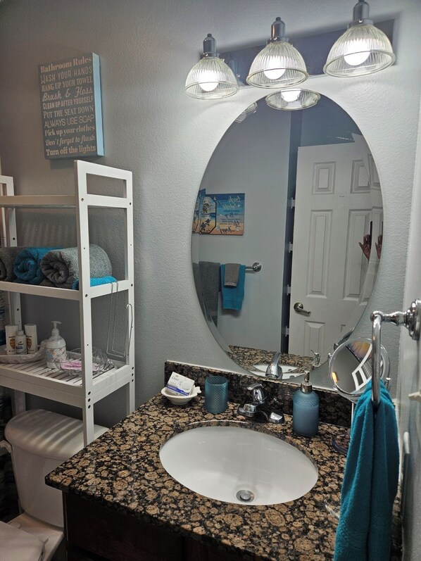 A bathroom with a white sink, granite countertop, and a large mirror. There are towels on a rack, a soap dispenser, and a toothbrush holder. - 2BD/2 BR Water Front Condo ... Haven in the springs (Ocean Springs)