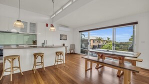 A modern kitchen with a central island, wooden flooring, and large windows offering a view of the outdoors.