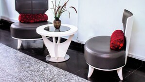 Eine moderne Lobby mit zwei schwarzen Ledersesseln, einer mit einer roten Polka-Dot-Kissen und der andere mit einem einfarbig roten Kissen, einem kleinen runden Tisch mit einer Vase und einem an der Wand montierten Flachbildfernseher.