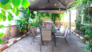 Eine Terrassenanlage im Freien mit Tisch und Stühlen, umgeben von Grünpflanzen und einem Pflasterboden.