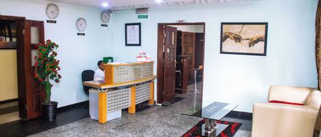 A reception area with a reception desk, a plant, a clock, and a framed artwork on the wall.
