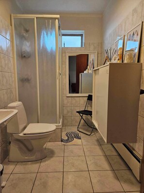 Un baño pequeño con inodoro, ducha y un ventanal.