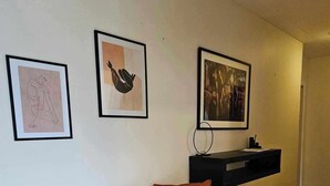 A modern living room with a black sofa, two orange cushions, and a black coffee table. There are three framed artworks on the wall.