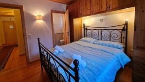 Una habitación con paneles de madera, una cama, una puerta y una lámpara fijada a la pared.