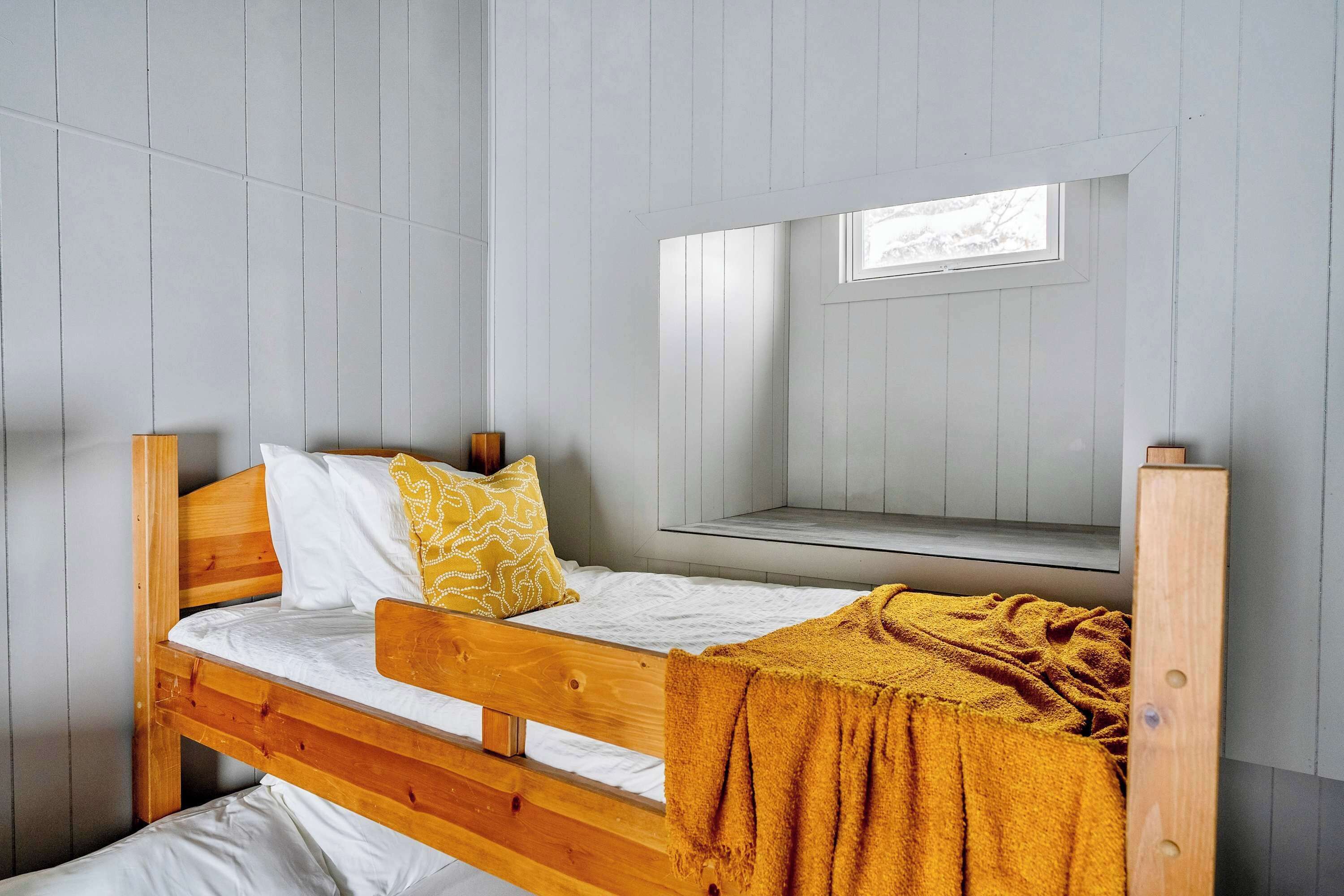 A bunk bed with a wooden frame, white bedding, and a mustard-colored blanket.
