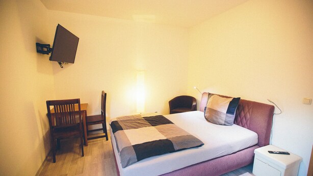 A bedroom with a bed, bedside table, chair, and a mounted TV. - Room with queen size bed and bathroom, tv, Netflix, wifi (Rudolstadt)