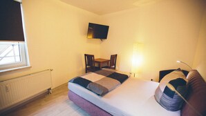A bedroom with a bed, a TV mounted on the wall, a window, a chair, and a bedside table. - Room with queen size bed and bathroom, tv, Netflix, wifi (Rudolstadt)