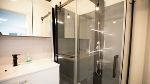 A modern bathroom with a glass-enclosed shower, a white vanity, and a mirror above the sink. - Deluxe Double Studio with kitchen line, bathroom, Shower, Toilet & king bed (Rudolstadt)