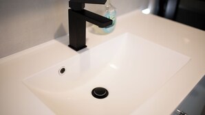 A white bathroom sink with a black faucet and a soap dispenser in the background. - Deluxe Double Studio with kitchen line, bathroom, Shower, Toilet & king bed (Rudolstadt)