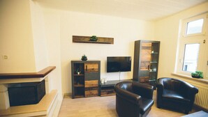 Ein Wohnzimmer mit Kamin, Ledersofas, einem Flachbildfernseher und Holzregalen.