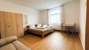 A bedroom with a wooden bed, a wooden wardrobe, a desk with a chair, and a window with curtains.