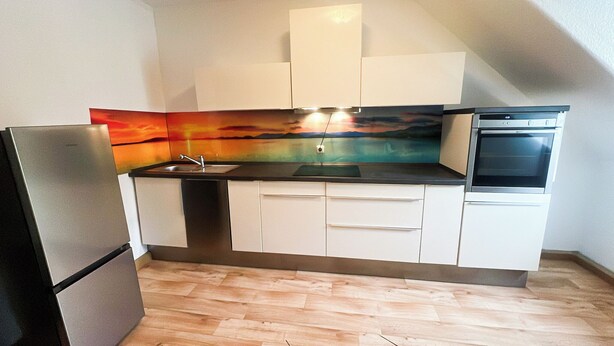 A compact kitchen with white cabinets, a stainless steel refrigerator, a built-in oven, and a colorful backsplash.