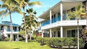 Ein Hotel mit zwei Etagen, Balkonen, Palmen und einem gepflegten Rasen.